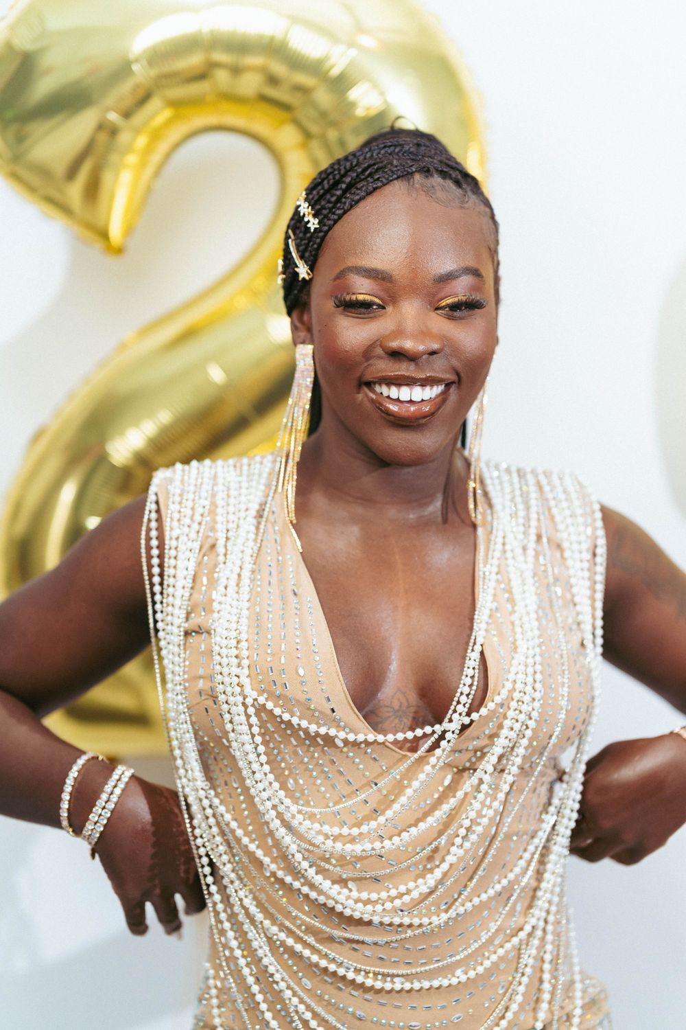Portrait in elegant pearl-adorned dress with gold balloon decorations in background.