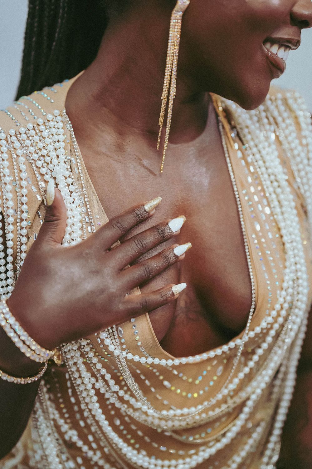 Close-up showing pearl necklace details and manicured hands against cream dress.
