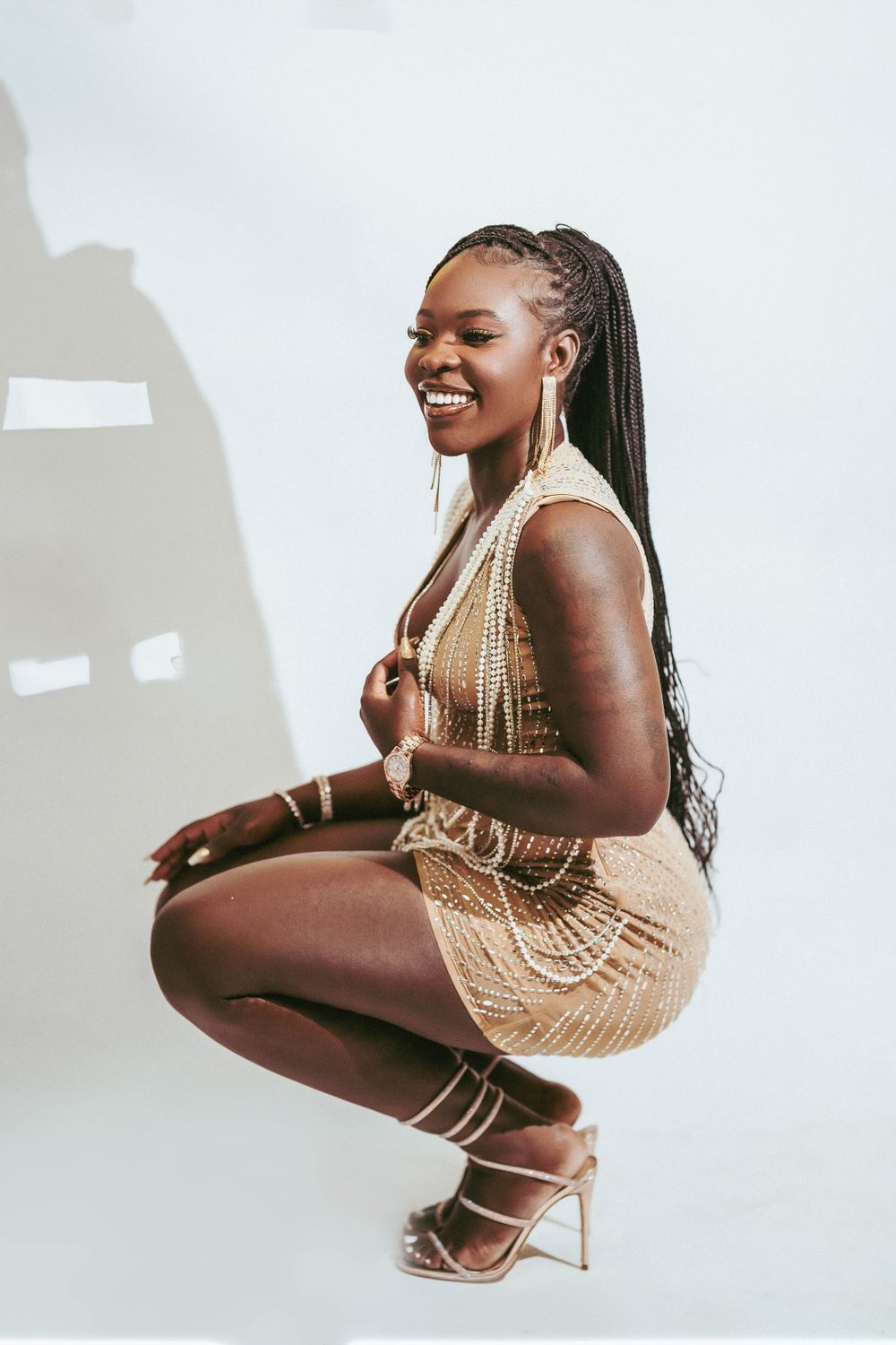 A glamorous model in gold sequin dress poses against white backdrop in fashion photoshoot series.