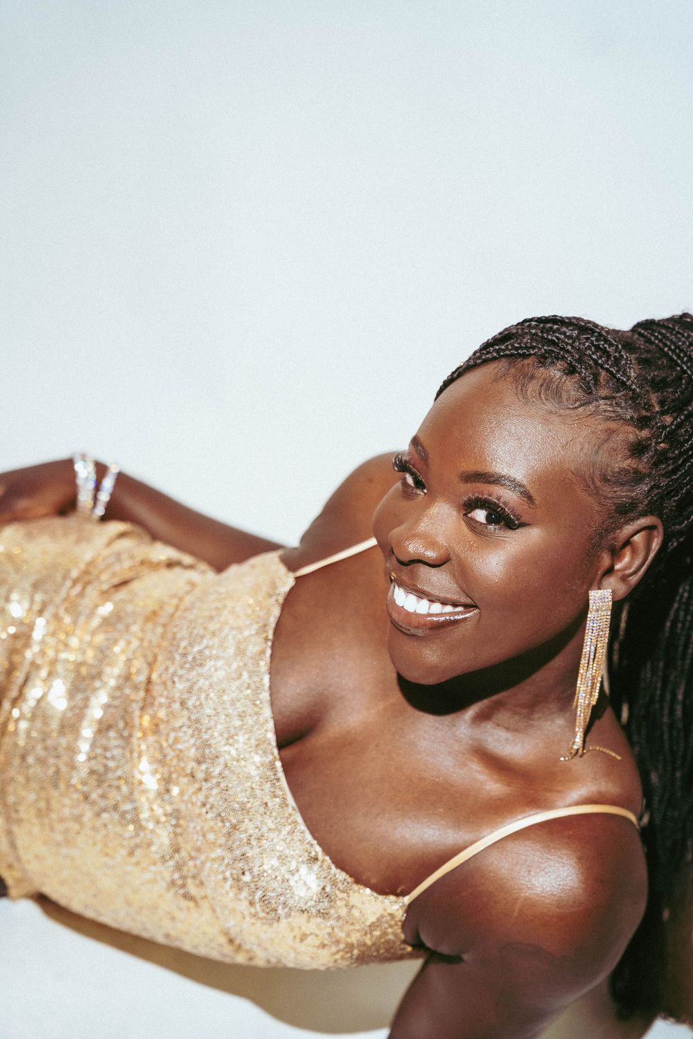 Close up shots of model wearing shimmering gold dress and dangle earrings in studio setting.