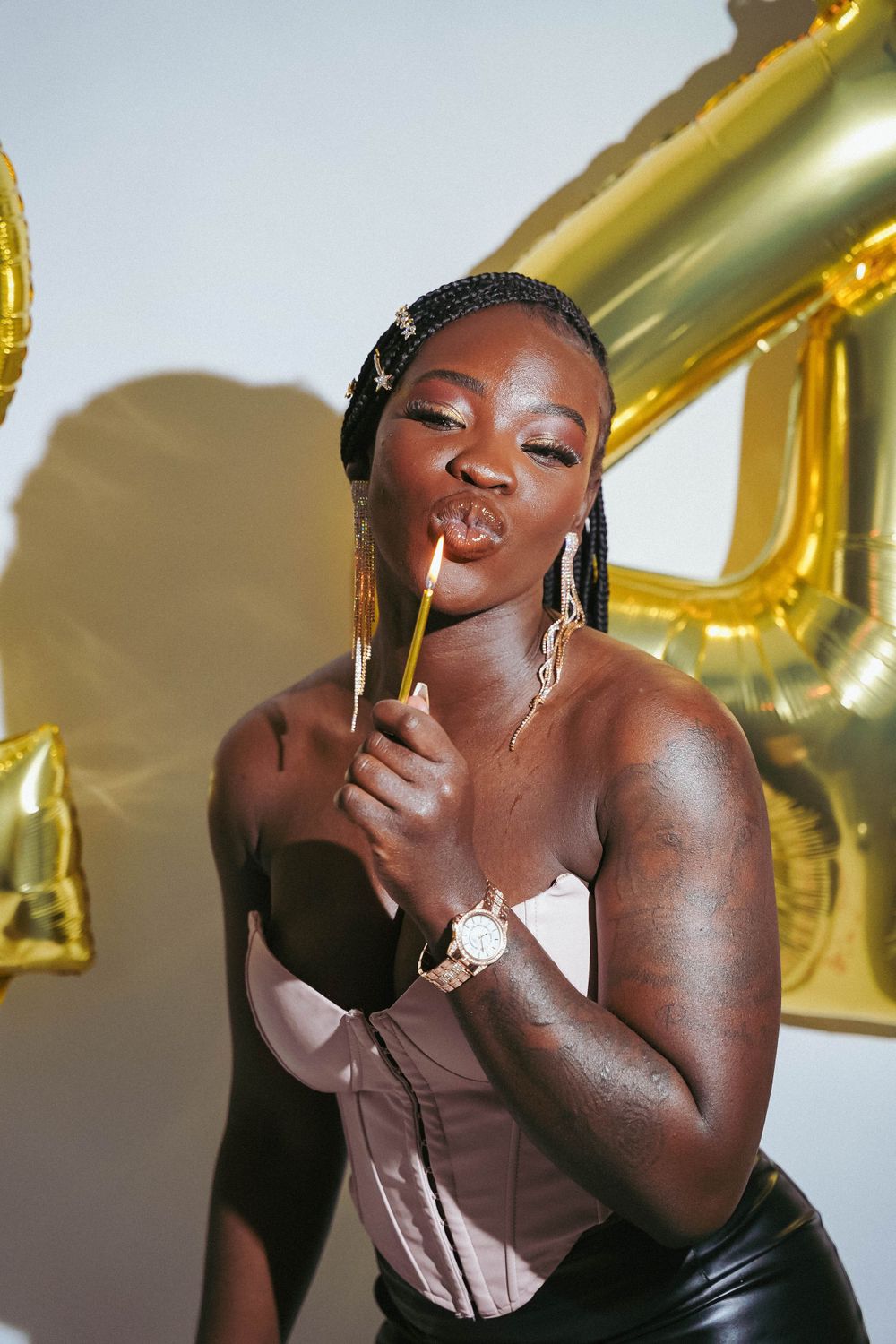 Fashionable woman in corset poses against gold balloon backdrop.