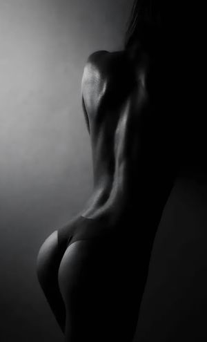 Black and white artistic photo of womans muscular back and figure in dramatic lighting.