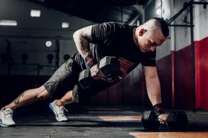 Tattooed male athlete performing dumbbell row exercise in dark gym setting.