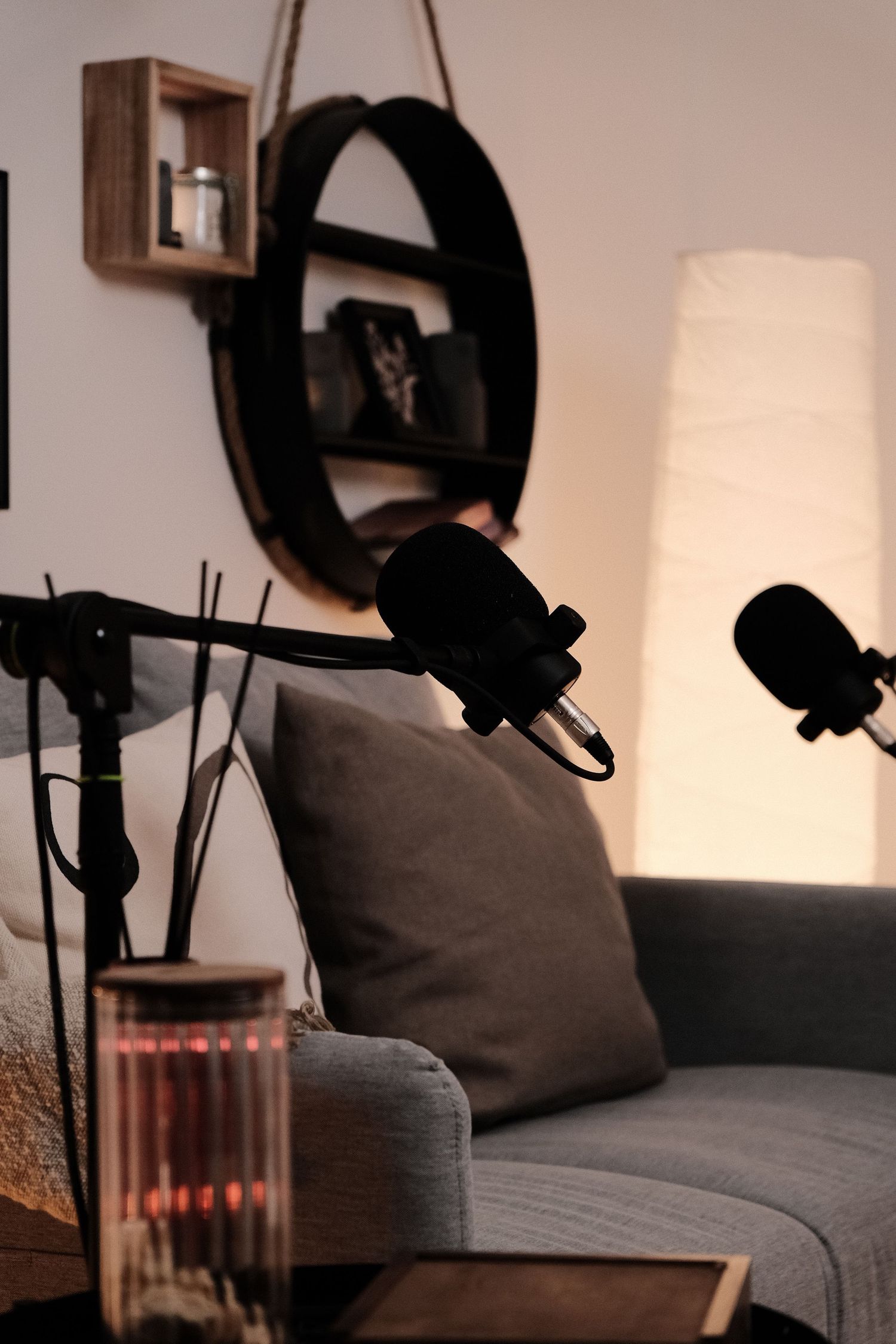 Professional podcast recording setup with microphones and cozy grey couch in a dimly lit room.