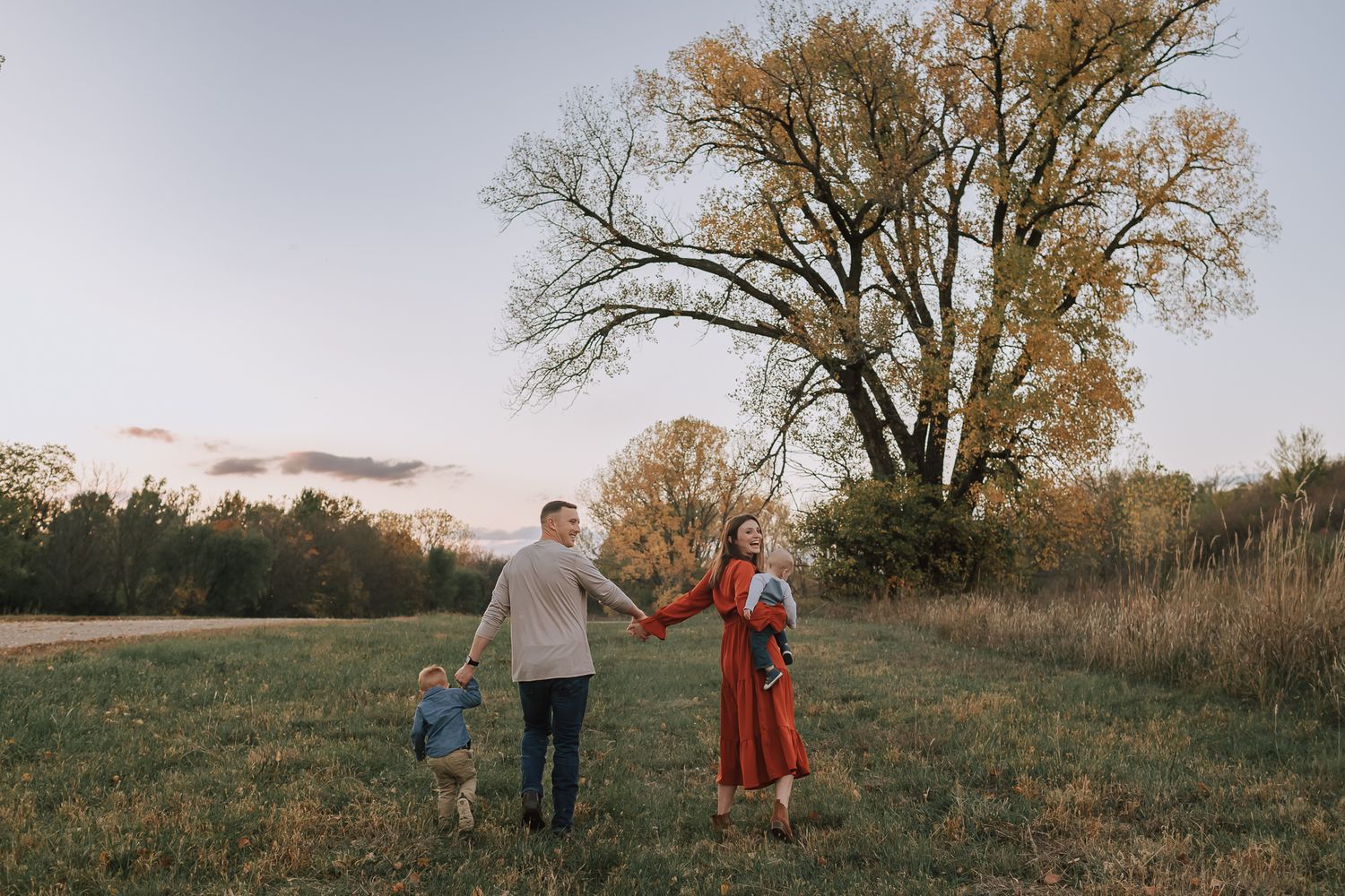 family holding hands walking towards a big tree changing colors for the fall