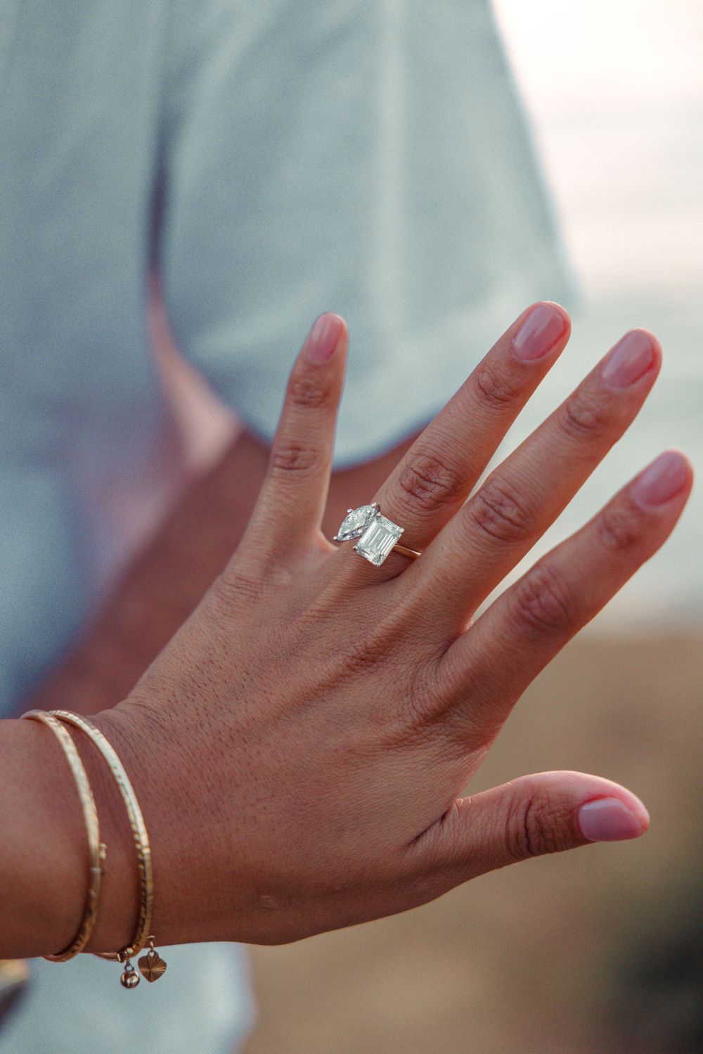 Close up of a hand wearing an elegant emerald cut diamond engagement ring and delicate bracelet.