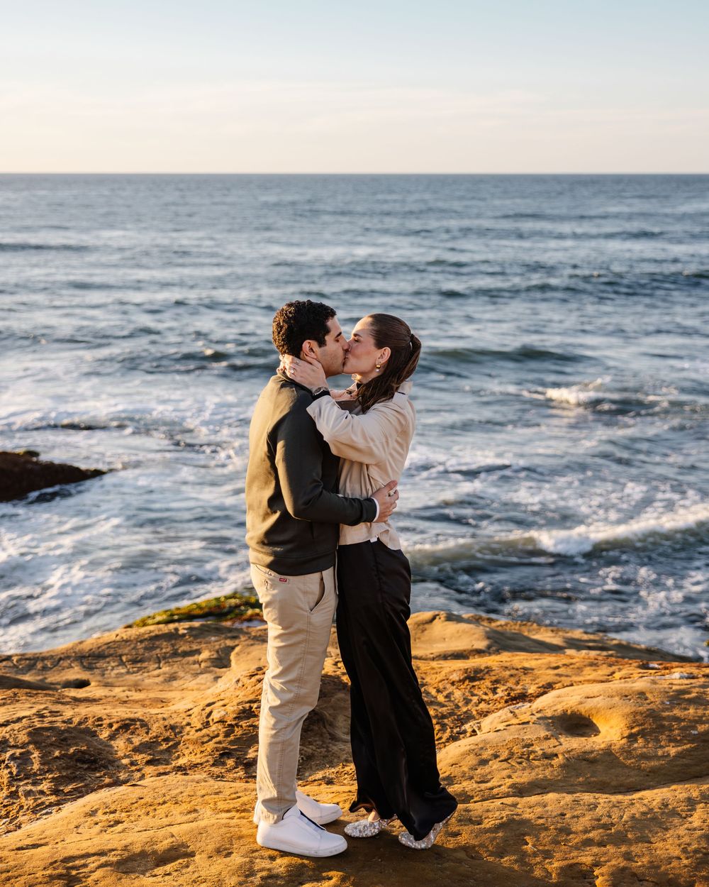 A romantic sunset photoshoot on a rocky coastal cliff overlooking the ocean waves.