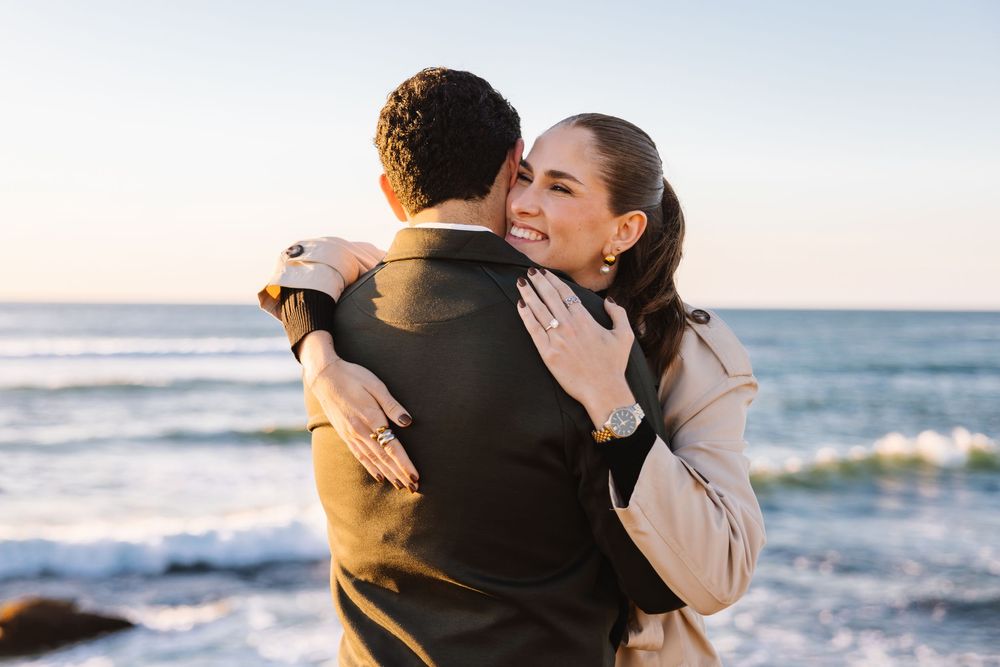 Couple embraces on a beach at sunset while waves crash on the shore in the background.