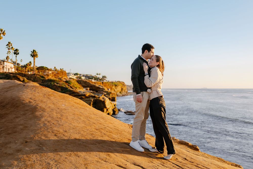 A couple embraces on a scenic coastal cliff at sunset overlooking the Pacific Ocean in Southern California.