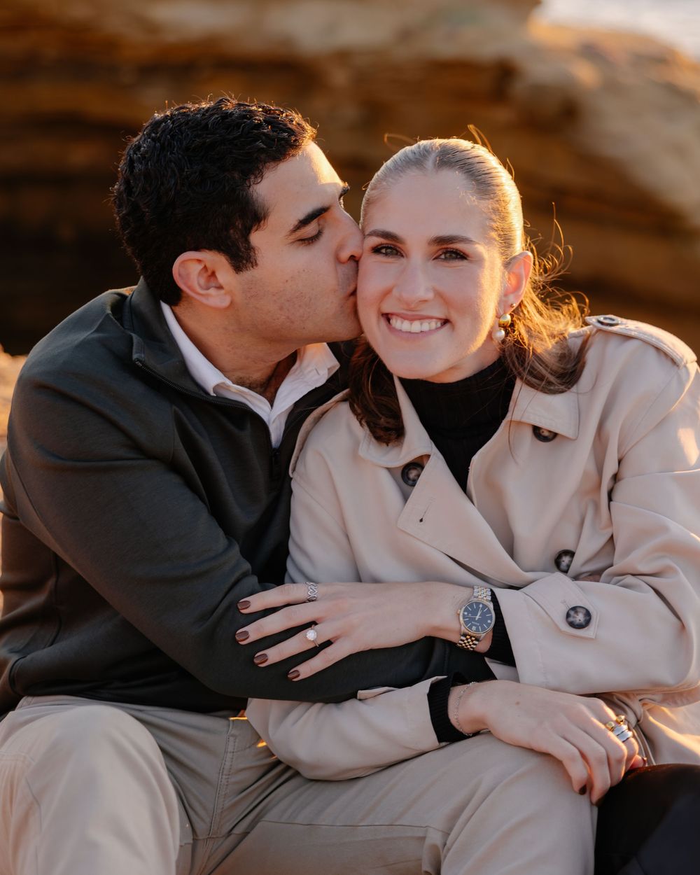 A romantic couple shares an intimate moment during golden hour as they embrace while sitting outdoors.