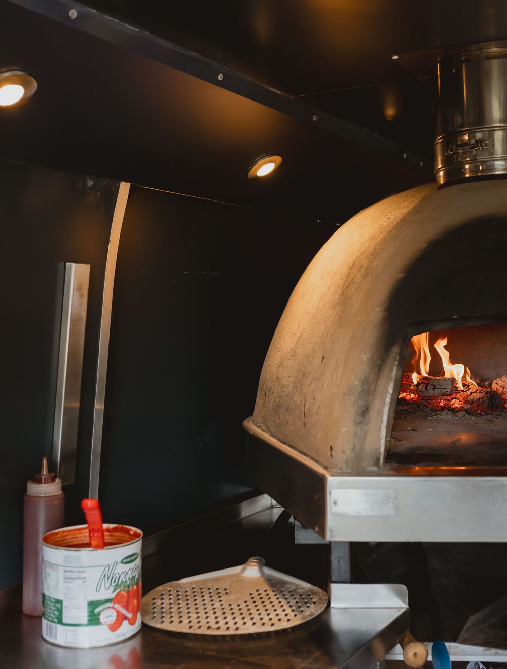 Wood-fired pizza oven with flames inside a dark commercial kitchen setup.