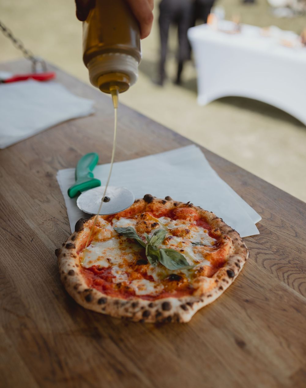 Olive oil being drizzled over a fresh Neapolitan margherita pizza on a wooden board.