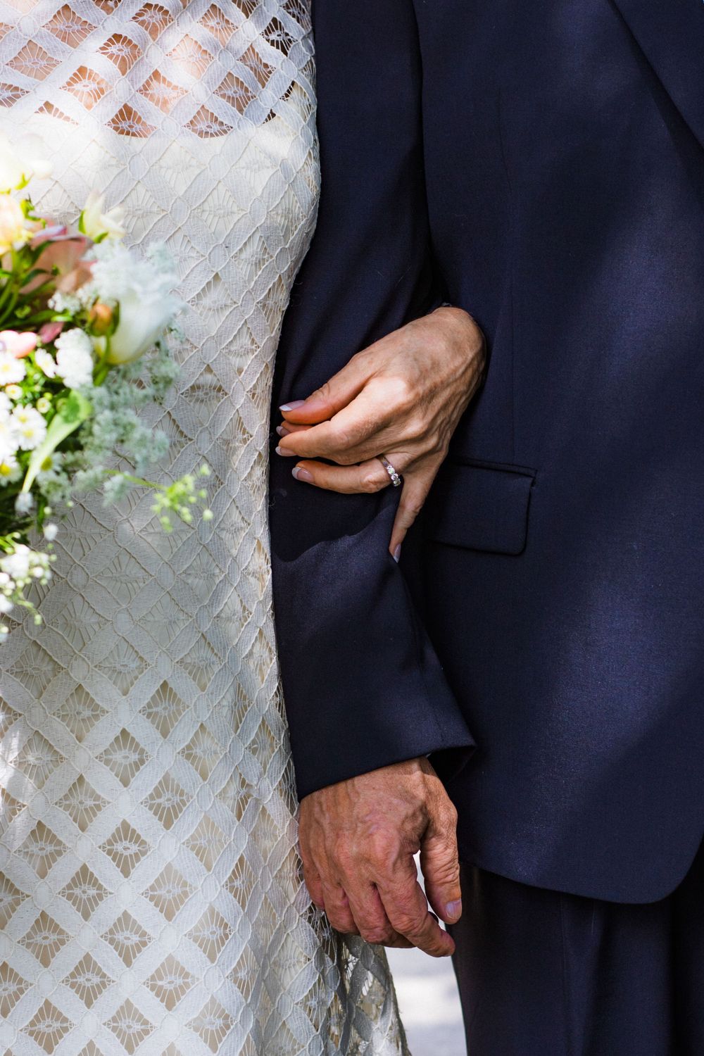 Detail of a white lace wedding dress against a dark suit.