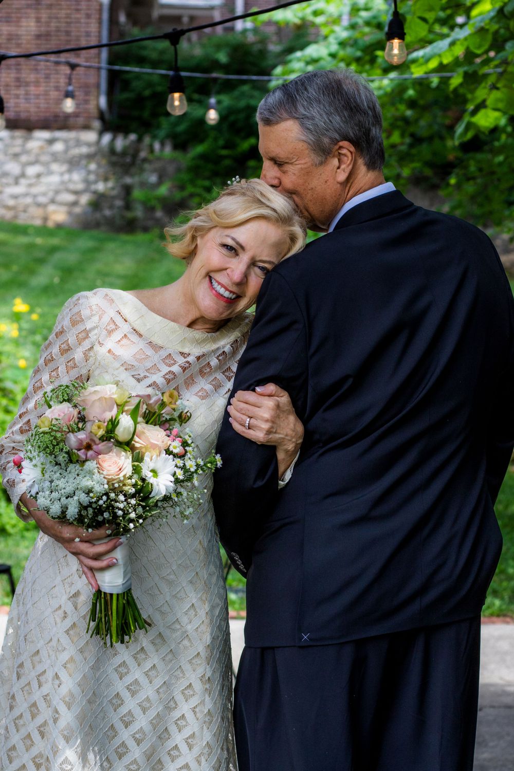 Wedding couple poses outdoors with a bouquet of pink and white flowers.