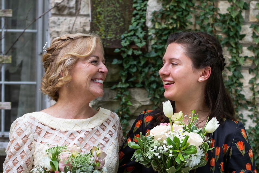 Wedding party laughs together in front of an ivy-covered building.