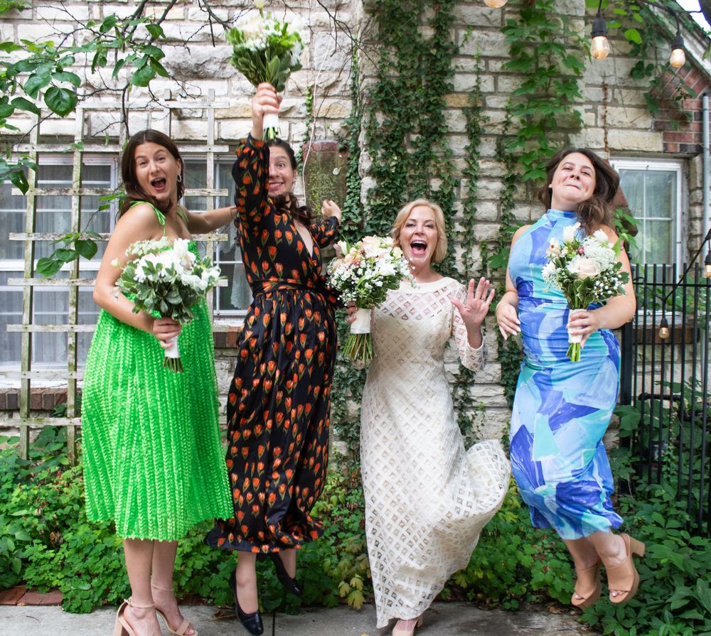 Wedding party in colorful dresses poses playfully in a garden setting.