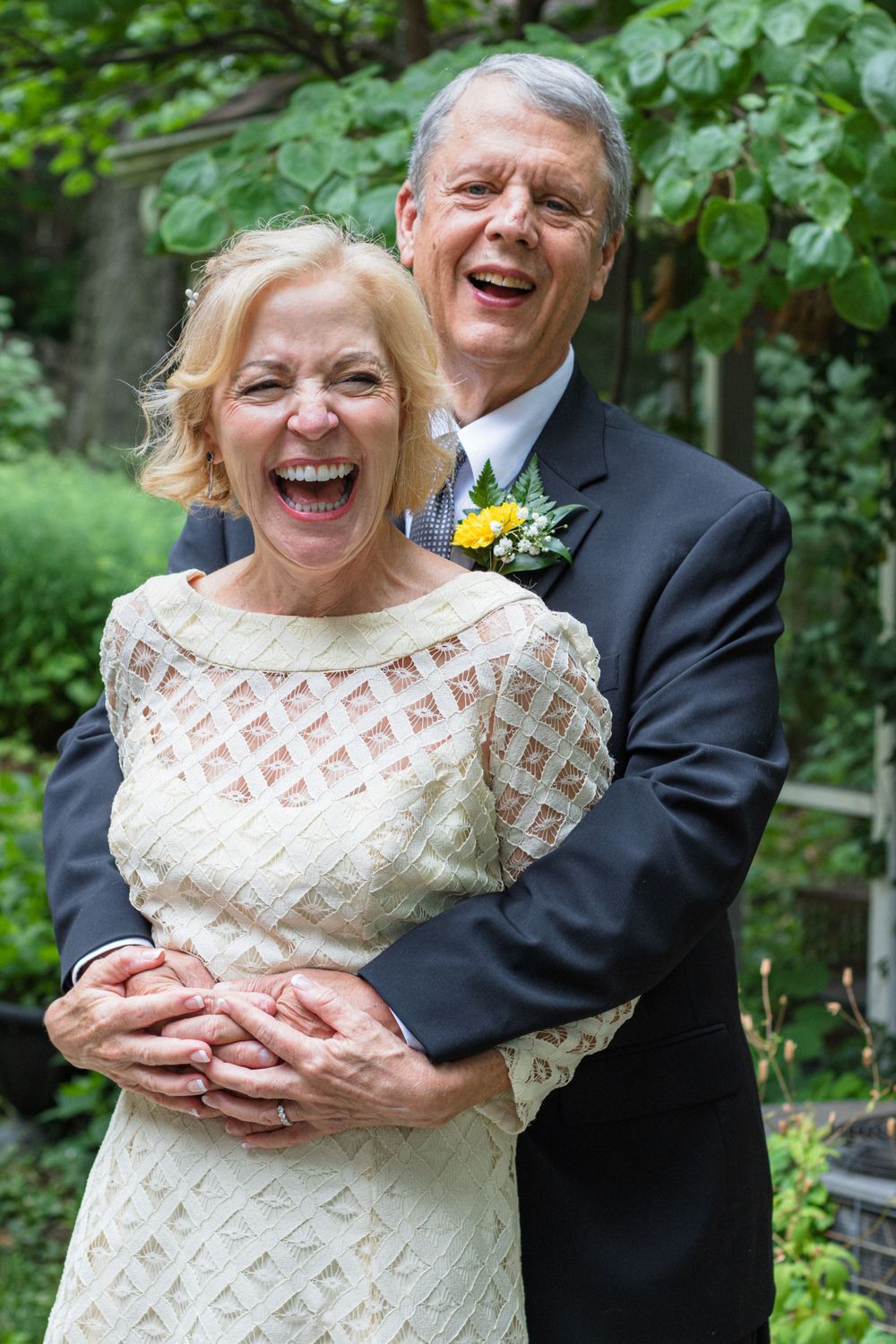 A couple shares a joyful embrace outdoors while wearing formal wedding attire.