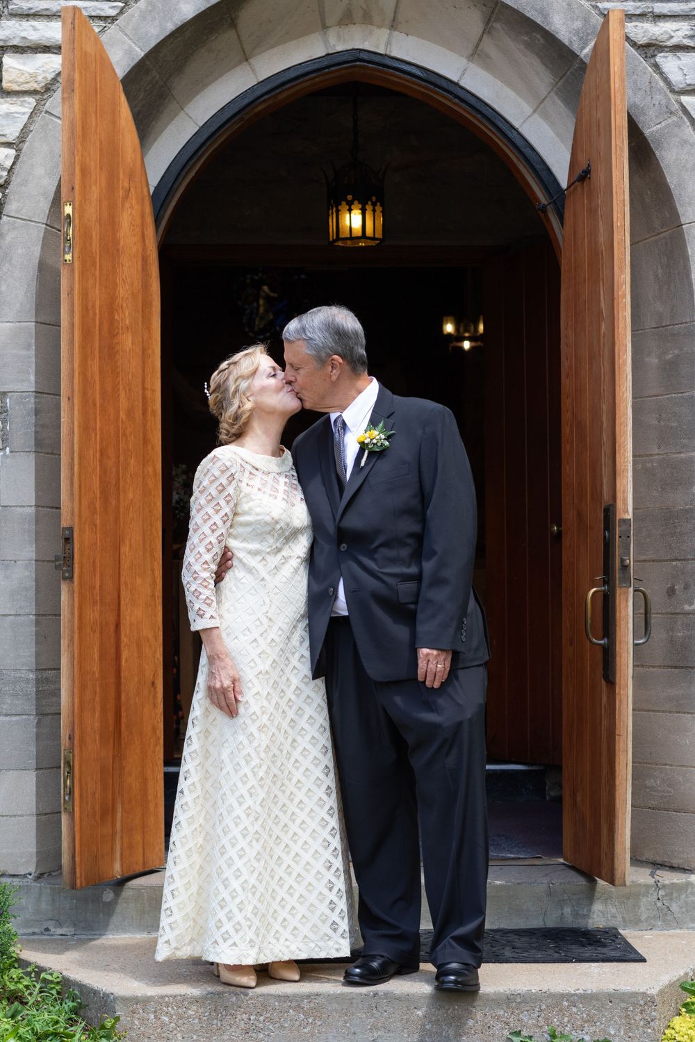A couple shares an intimate moment under stone archways with wooden doors.