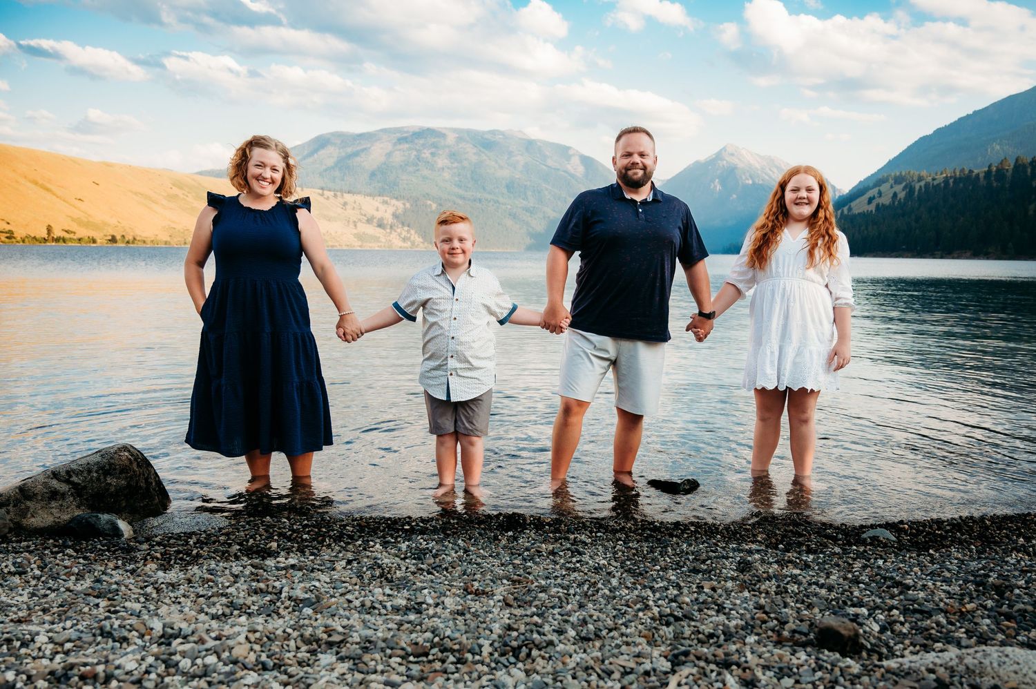 A family stands together holding hands at the edge of a mountain lake at sunset.  Wallowa Lake, Joseph, Oregon