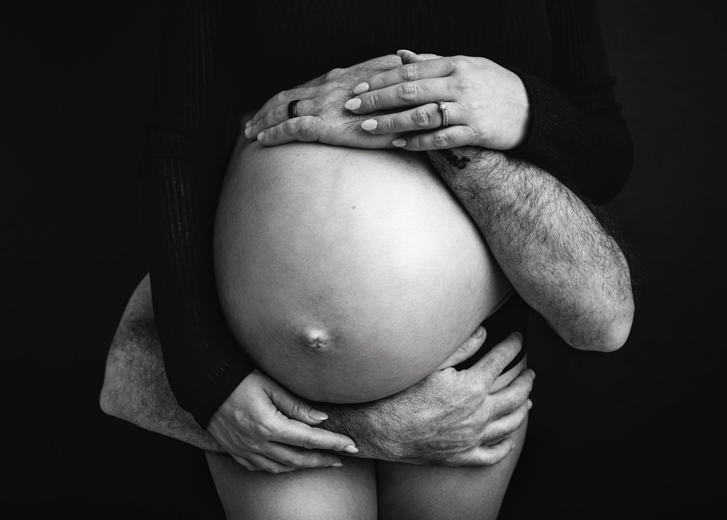 Black and white artistic photograph of hands cradling pregnant belly.