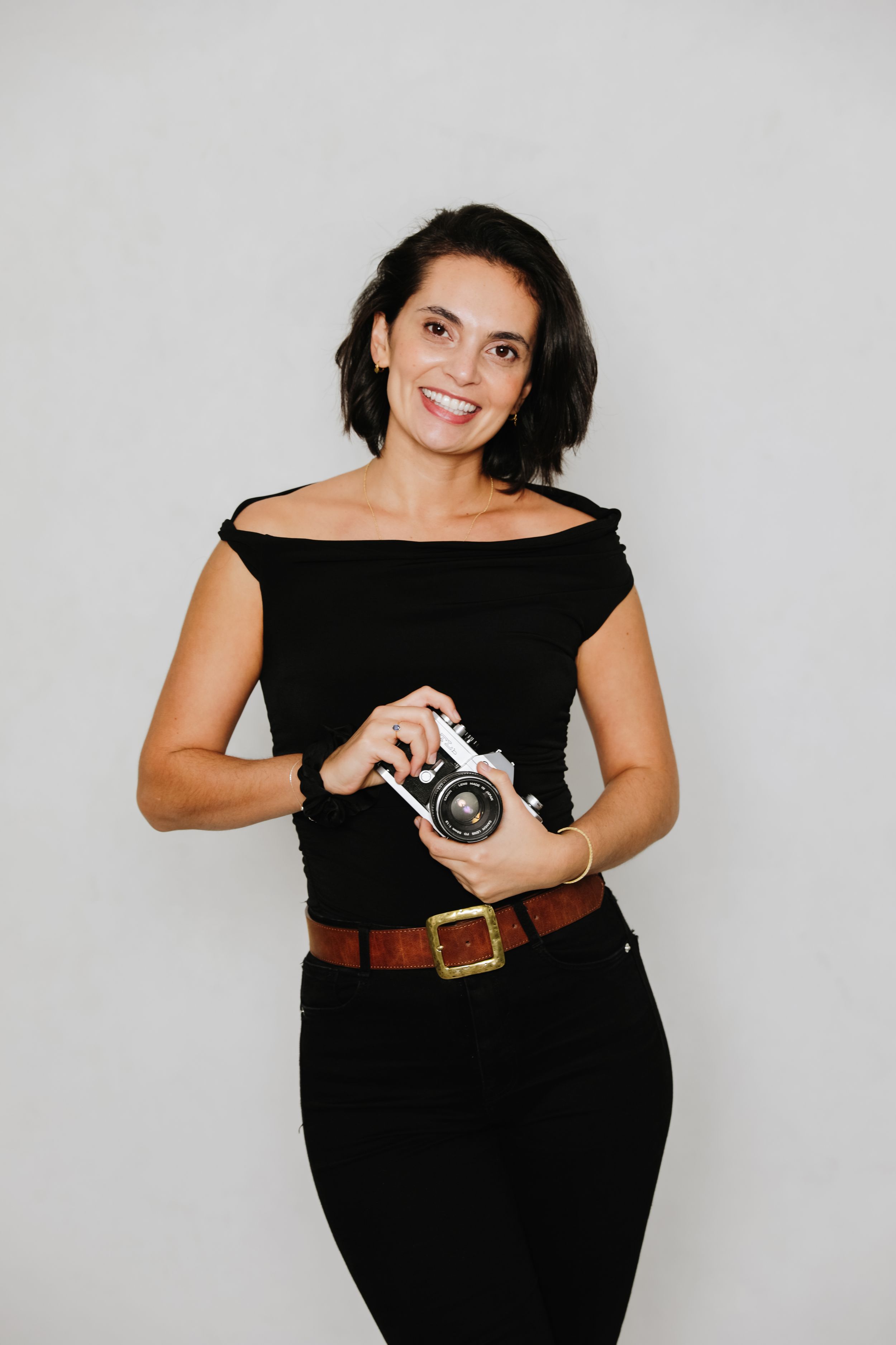 Professional photographer in black dress holding vintage camera against grey background.