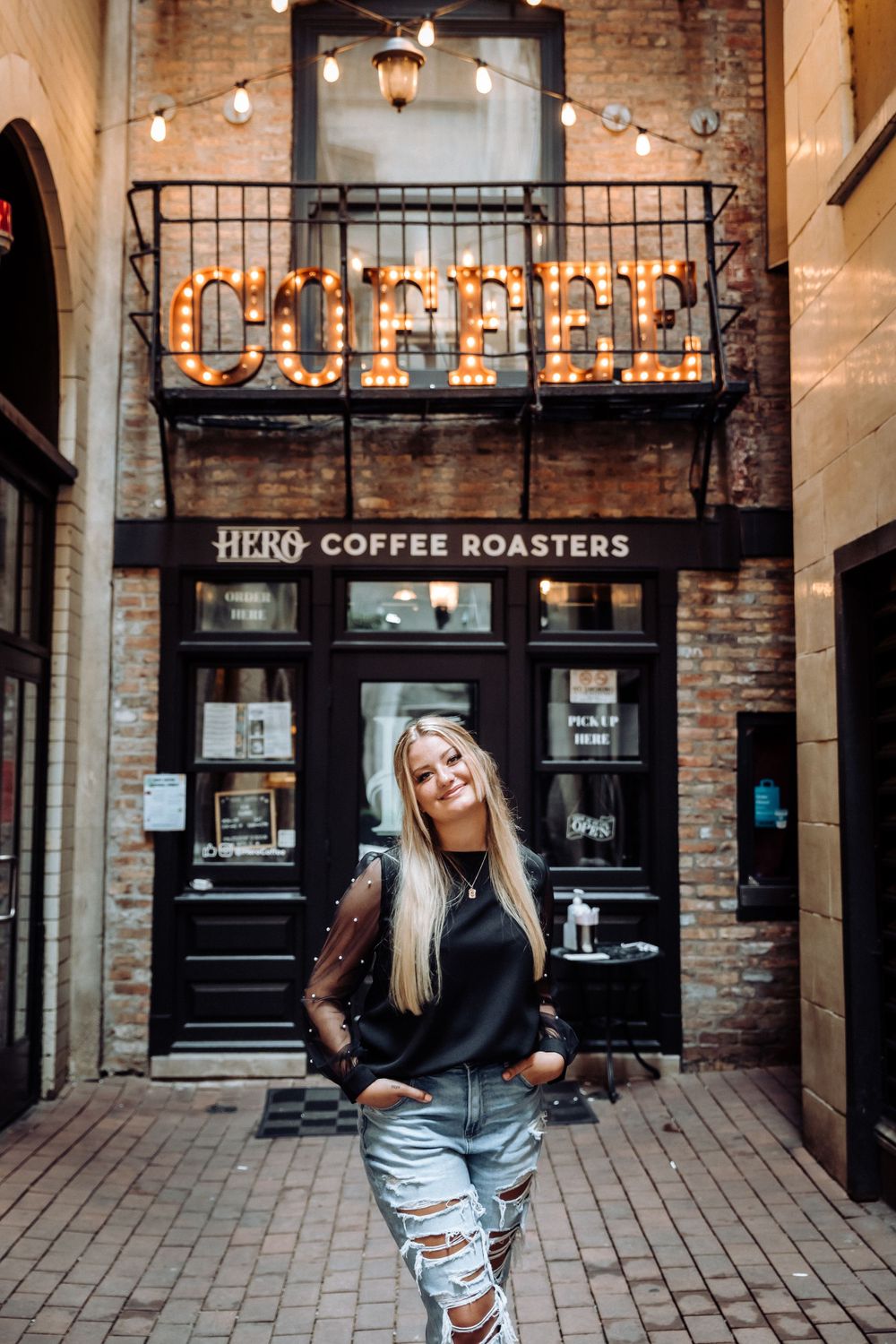 Casual street style portrait in front of Hero Coffee Roasters brick storefront.