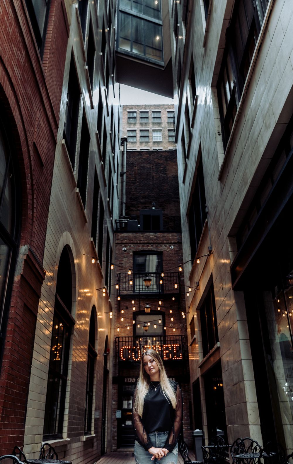 A moody architectural shot of a narrow urban alley with brick walls and hanging lights creating dramatic atmosphere.