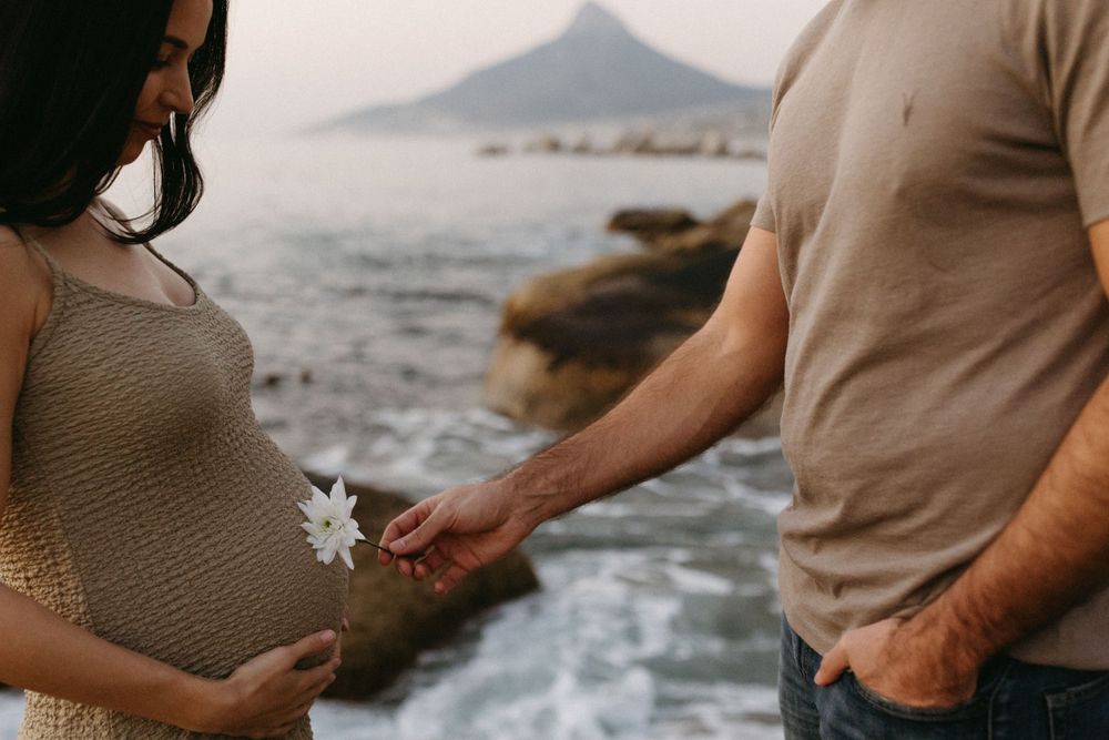 Expectant couple sharing tender moments by the ocean.