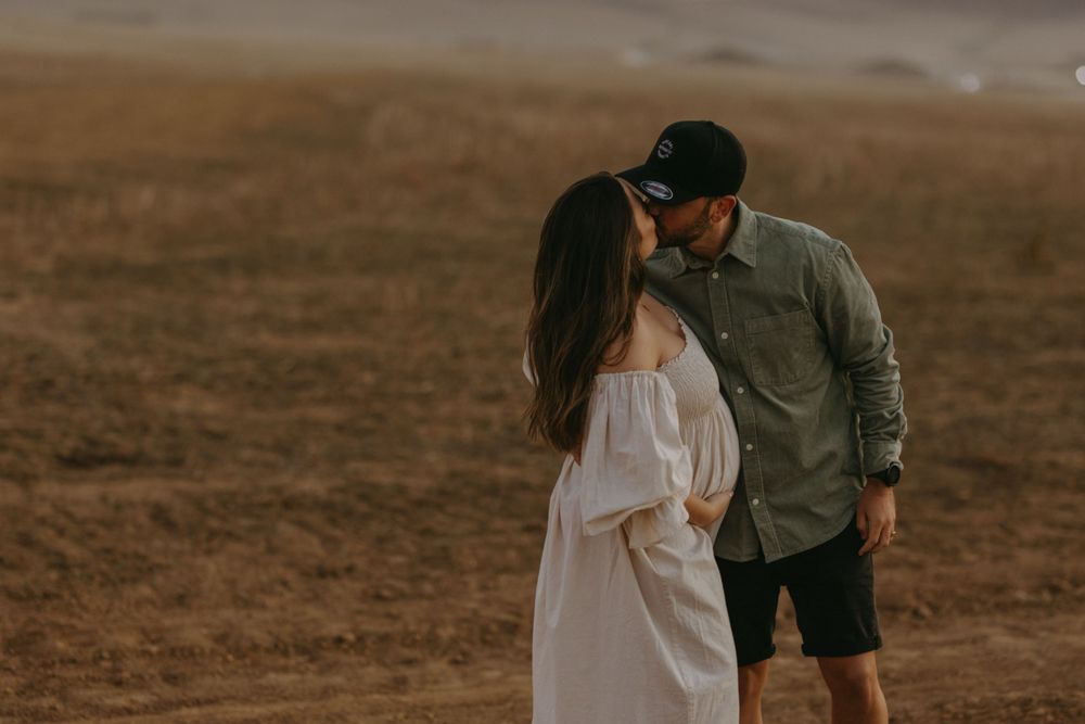 Romantic couple embracing on desert terrain at sunset.
