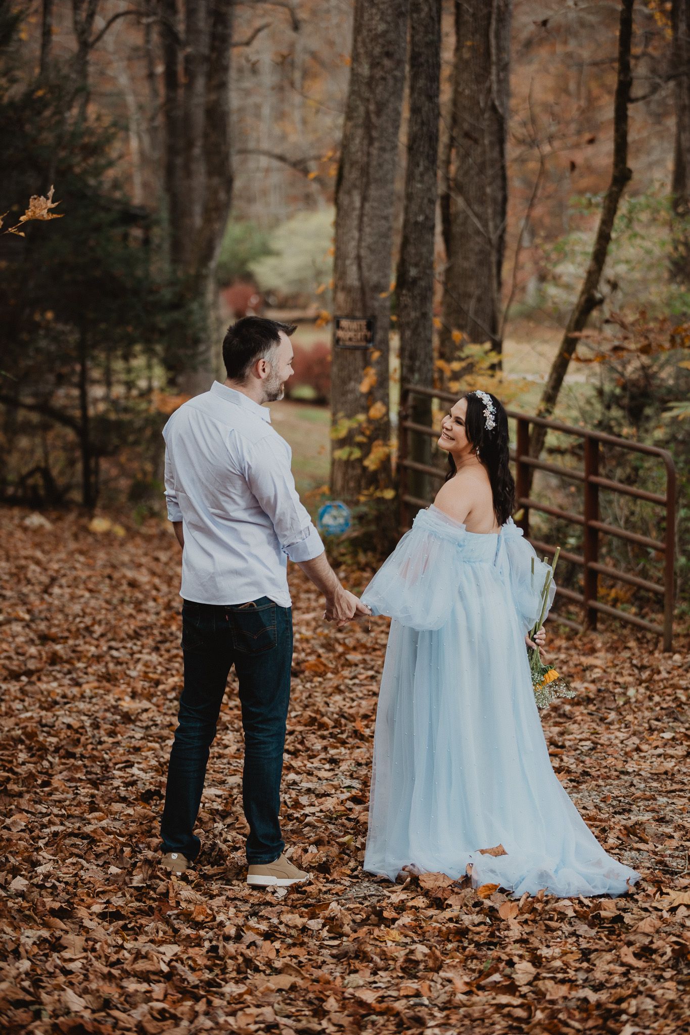 Romantic autumn photoshoot with couple in light blue dress among fallen leaves.