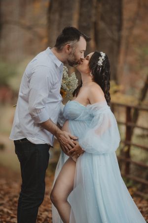 Romantic maternity photography session featuring a flowing light blue dress in a wooded setting.