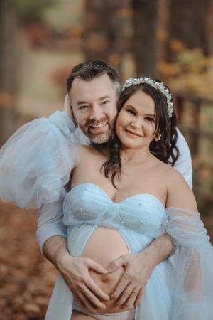 A couple shares intimate moments in an outdoor maternity photoshoot wearing a light blue gown.