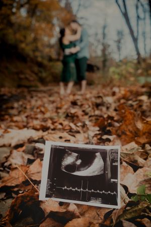 Ultrasound images laid out on fallen autumn leaves during a pregnancy announcement photoshoot.