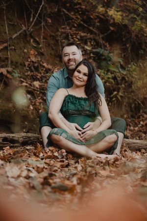 A romantic autumn photoshoot with a couple lying in fallen leaves wearing green and casual attire.