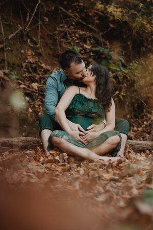 Couple in casual attire sharing tender moments while lying in autumn leaves.