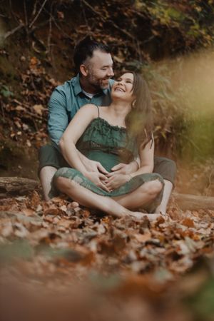 Romantic autumn photography session showing couple embracing on ground covered in fallen leaves.