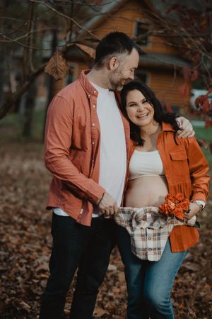 A couple in autumn attire embracing in a wooded area with fallen leaves during a photoshoot.