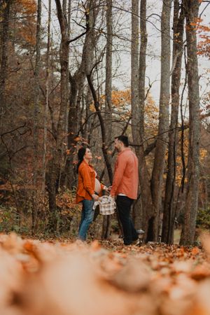 Autumn forest engagement session with couple walking through fallen orange leaves.