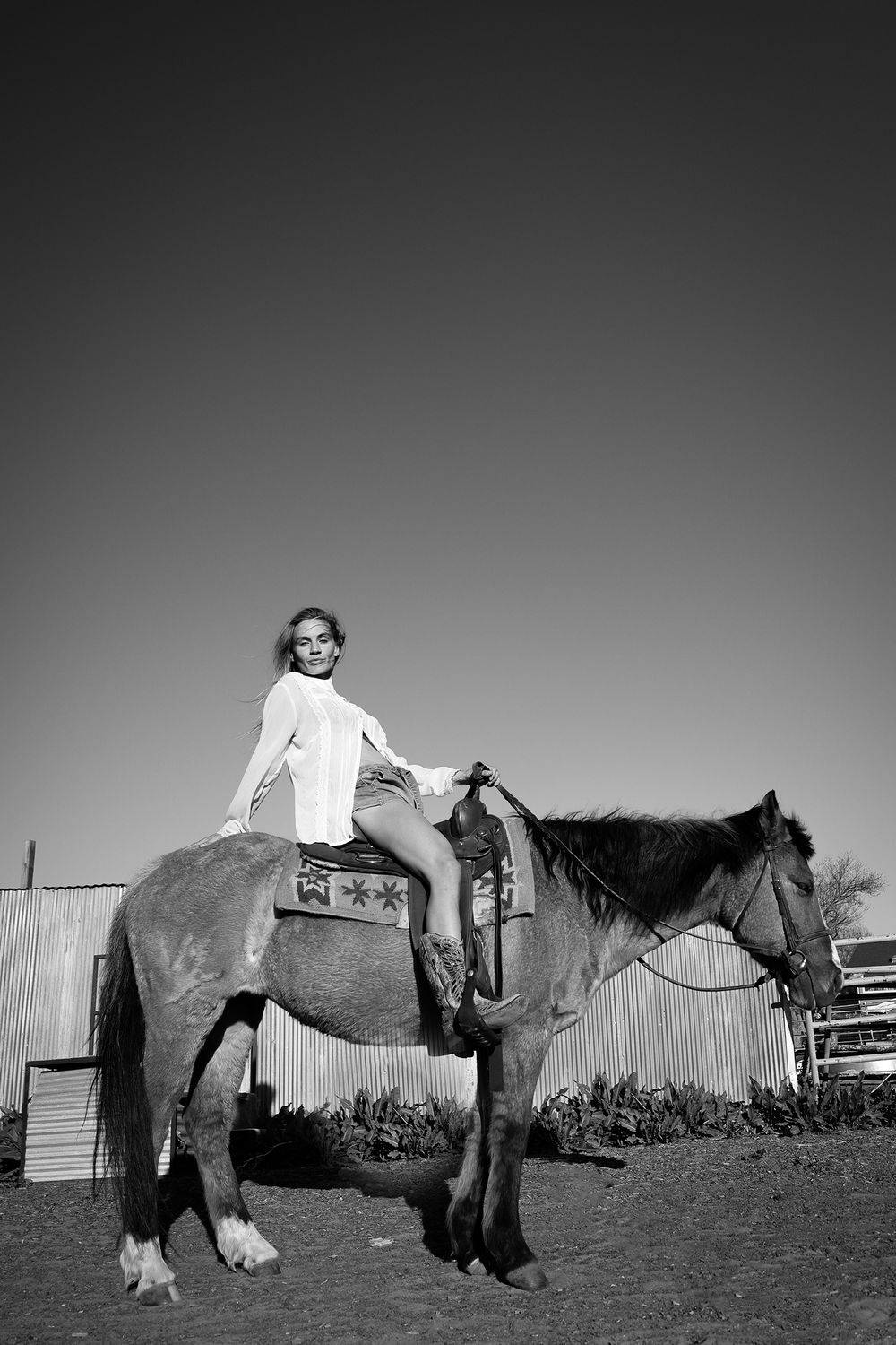 Young rider sits atop a saddled horse in rustic black and white farm setting.