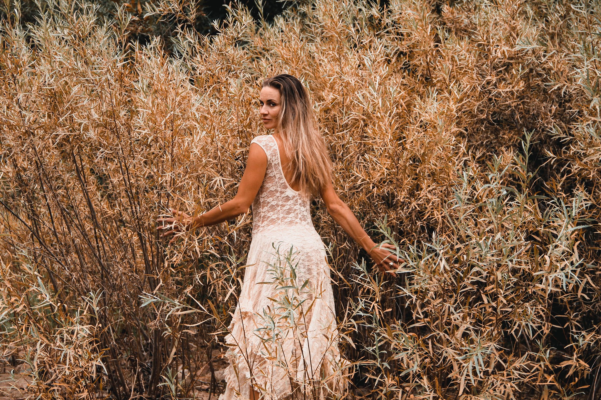 Model in white dress twirls among golden autumn grasses.