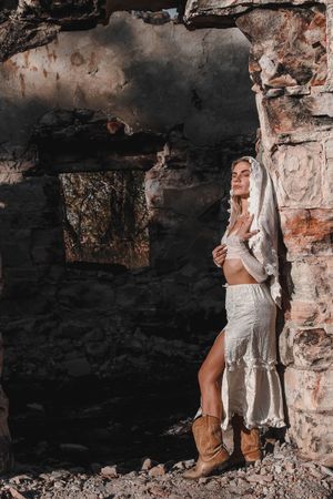Fashion shot against weathered stone wall with model in white dress and boots.