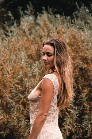 Woman in white lace dress poses near autumn foliage.