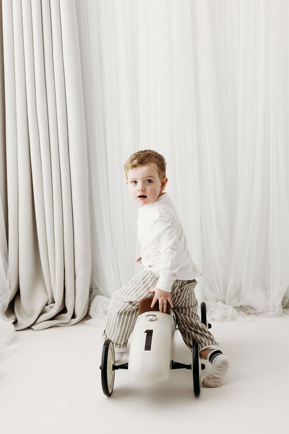 Smiling toddler sitting on a neutral backdrop during a studio photography session.