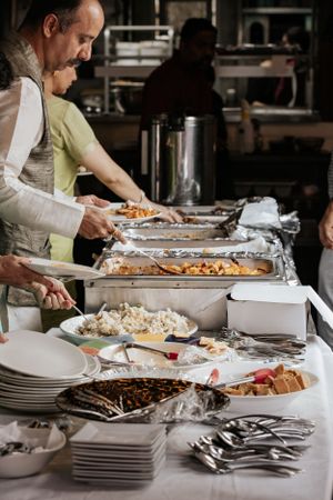 Guests serving themselves from a buffet spread of various dishes at a wedding reception catering table.