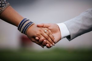 Close-up of a couple holding hands, showcasing blue bangles and a gold engagement ring.