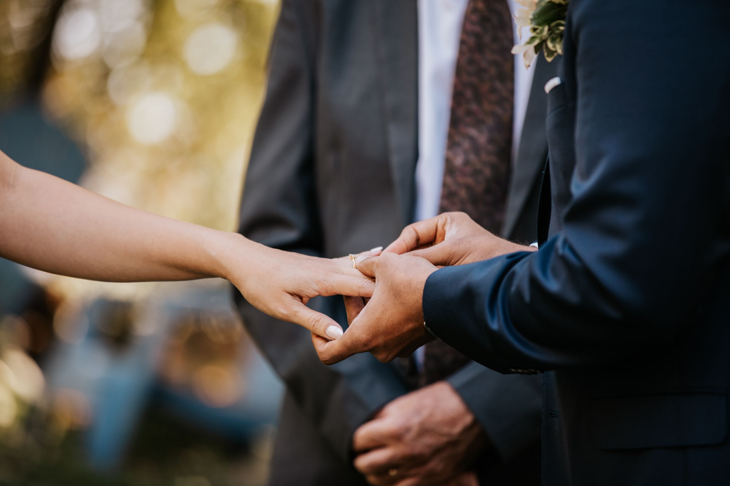 A groom places a wedding ring on his bride's finger during an outdoor ceremony.