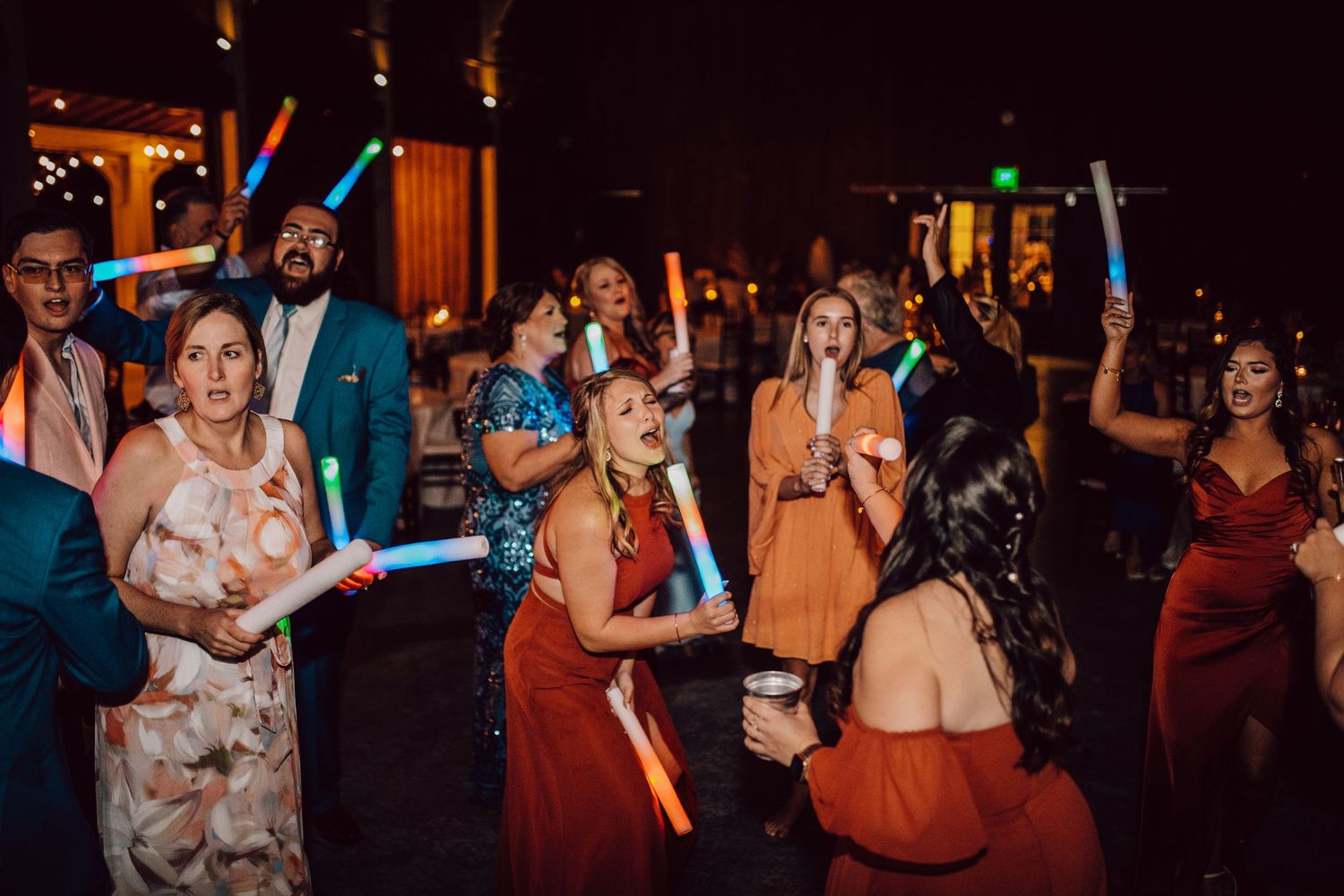Lively dance party scene with guests holding colorful light sticks under ambient lighting.