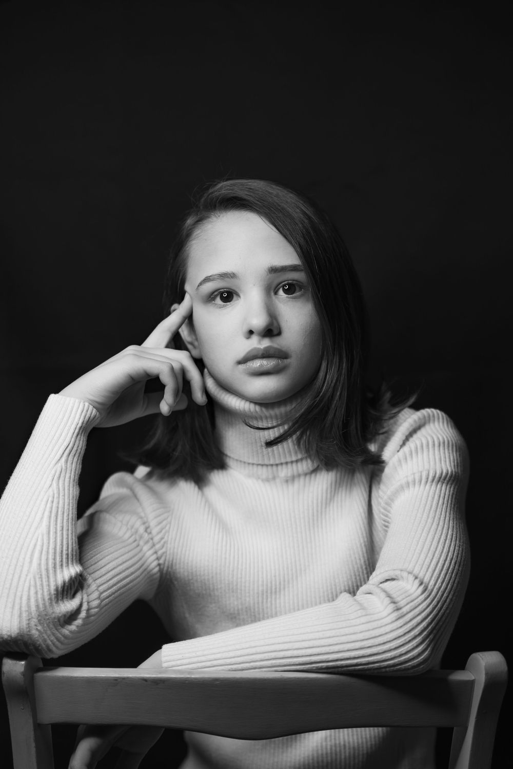 Young teen girl in turtleneck sweater posing thoughtfully in black and white portrait.