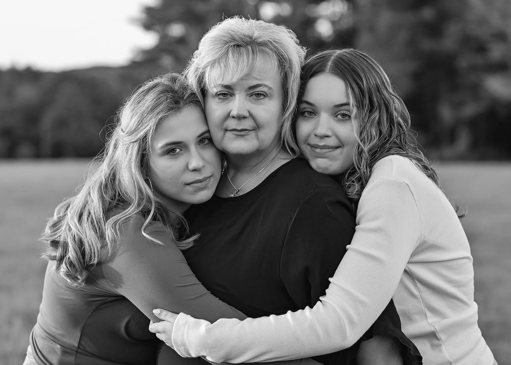 Black and white portrait of a mother and two daughters embracing warmly in an outdoor field setting.