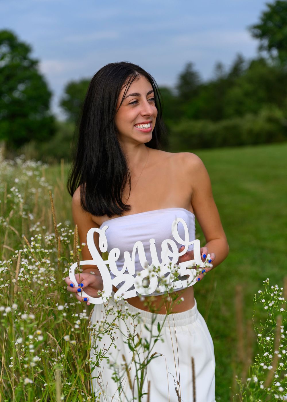 Smiling senior girl holding Class of 2023 sign in blooming wildflower field.